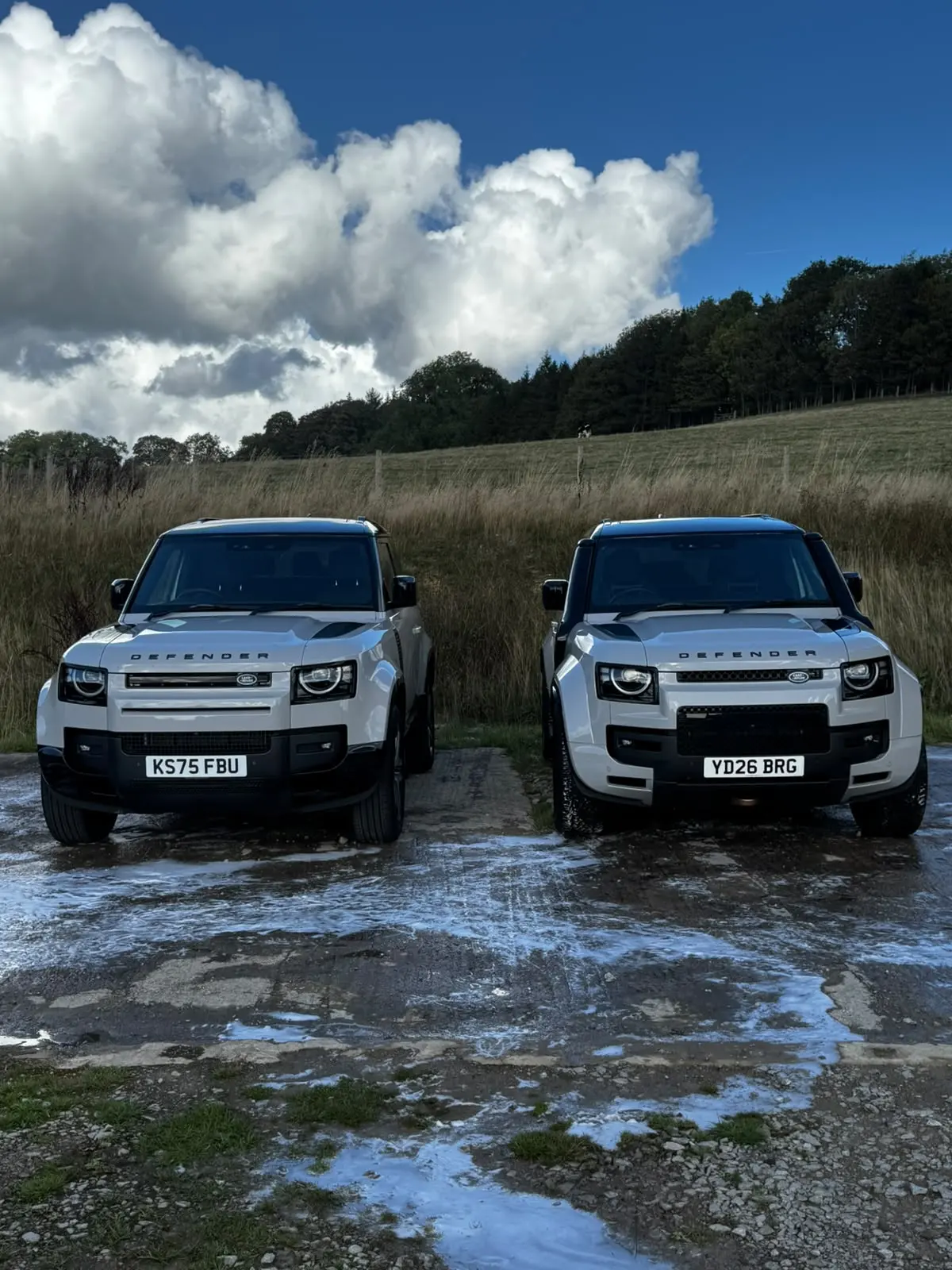 Two silver Land Rover Defenders parked nose-on beside a field after a maintenance wash in Harrogate