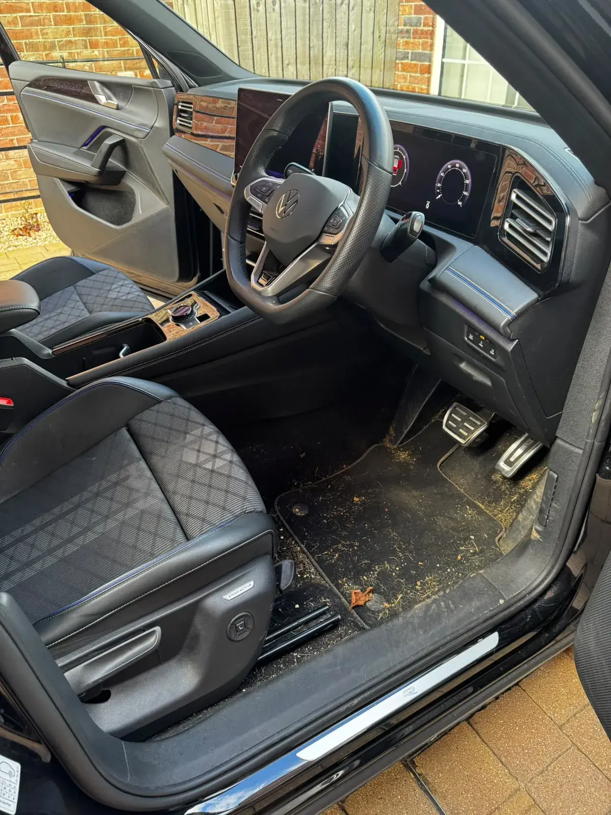 Front footwell of a Volkswagen Tiguan before cleaning, with grass and debris on the mat
